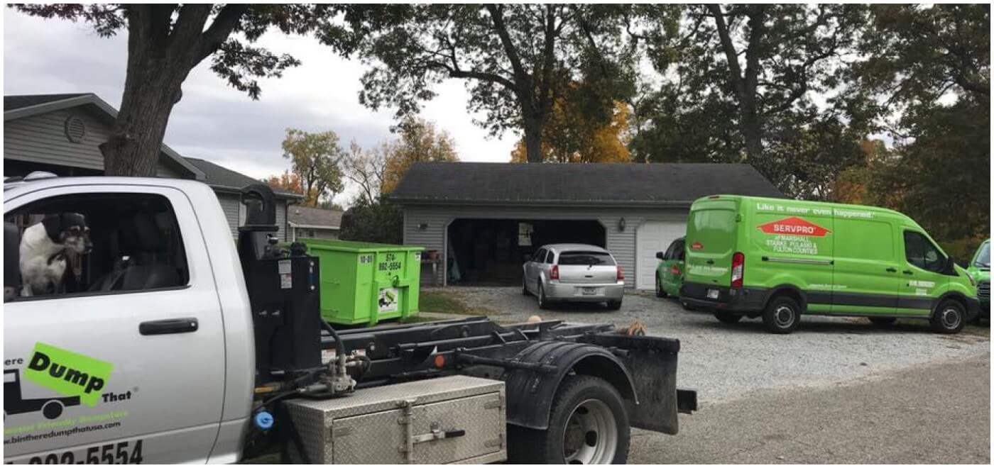 A residential driveway with various service vehicles including a junk hauling franchise truck and a cleaning service van.