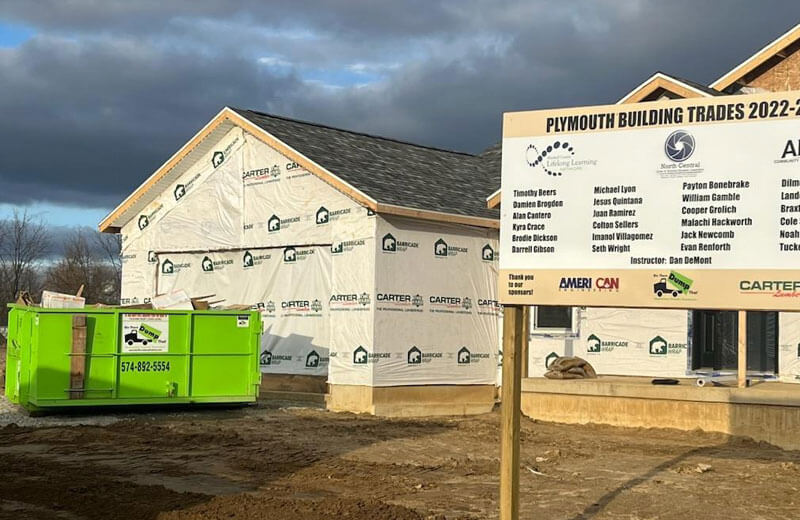 New residential construction site with partially completed houses and a dumpster rental franchise green dumpster in the foreground.