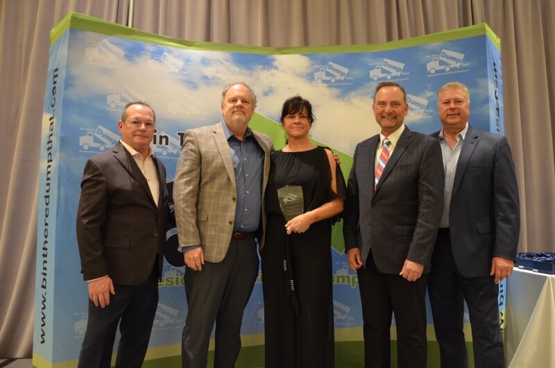 Four men and one woman posing for a photo at an award ceremony with a branded junk removal franchise backdrop.