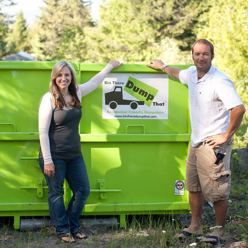 Two people standing next to a green dumpster, part of the "bin there dump that" junk removal franchise.