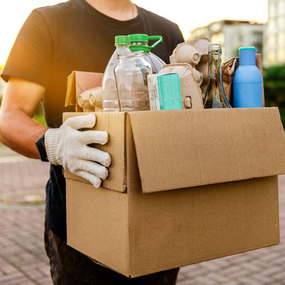 A man holds a box filled with garbage items