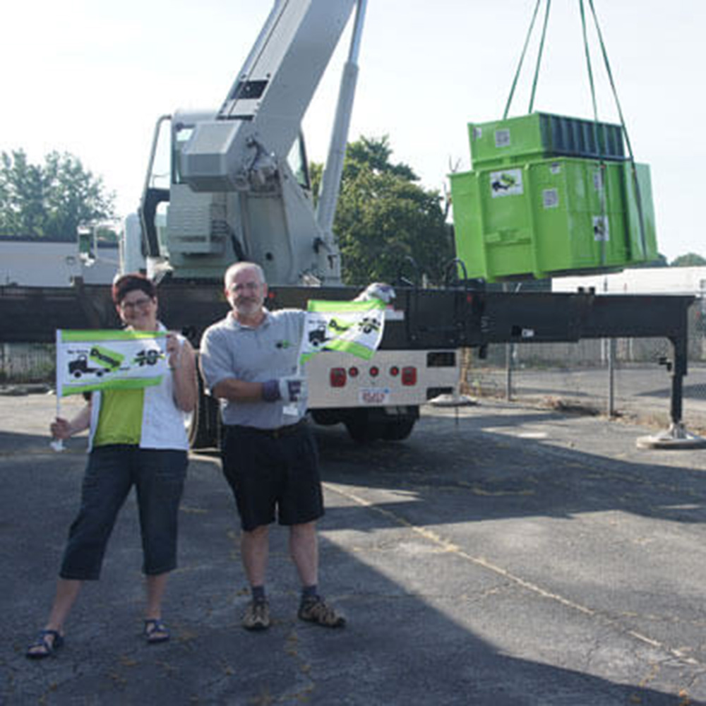 Two franchise operators hold a Bin there Dump That flag in front of a truck lifting a dumpster